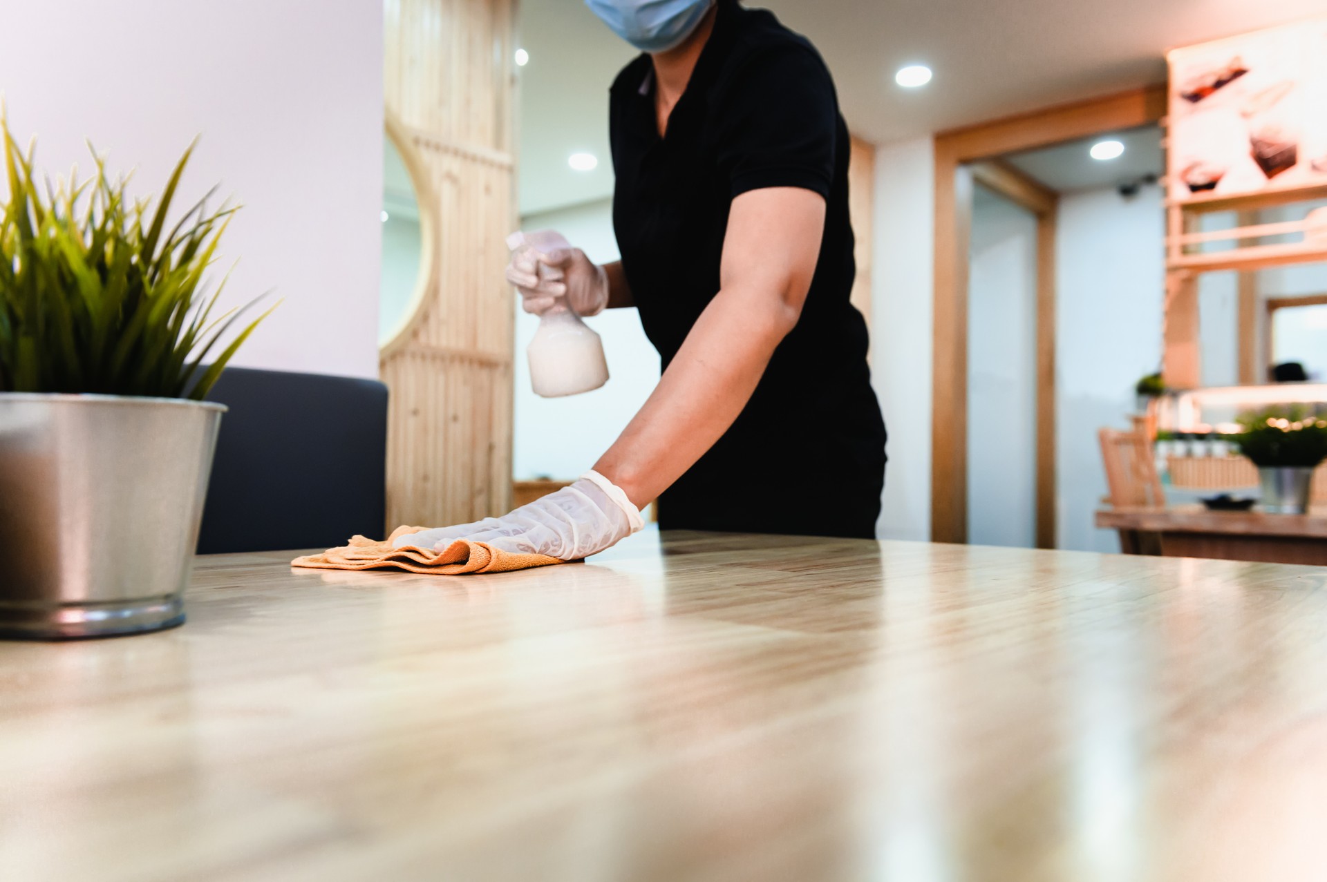 Hand of waiter woman cleaning table with disinfectant spray and microfiber cloth for disinfecting at indoor restaurant. Coronavirus prevention concept.