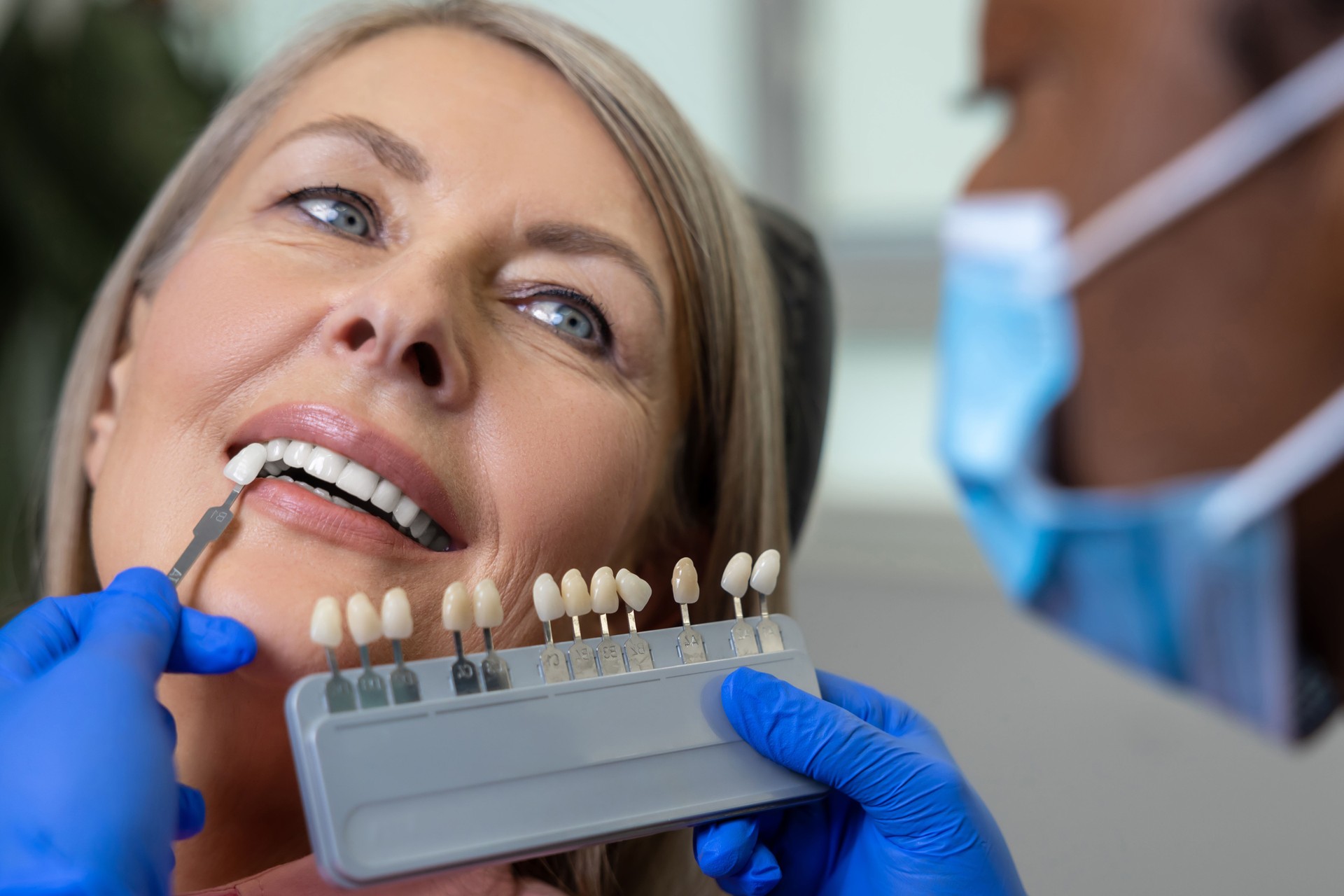 Woman patient with doctor orthodontist choosing the shade of dental veneer according to color chart