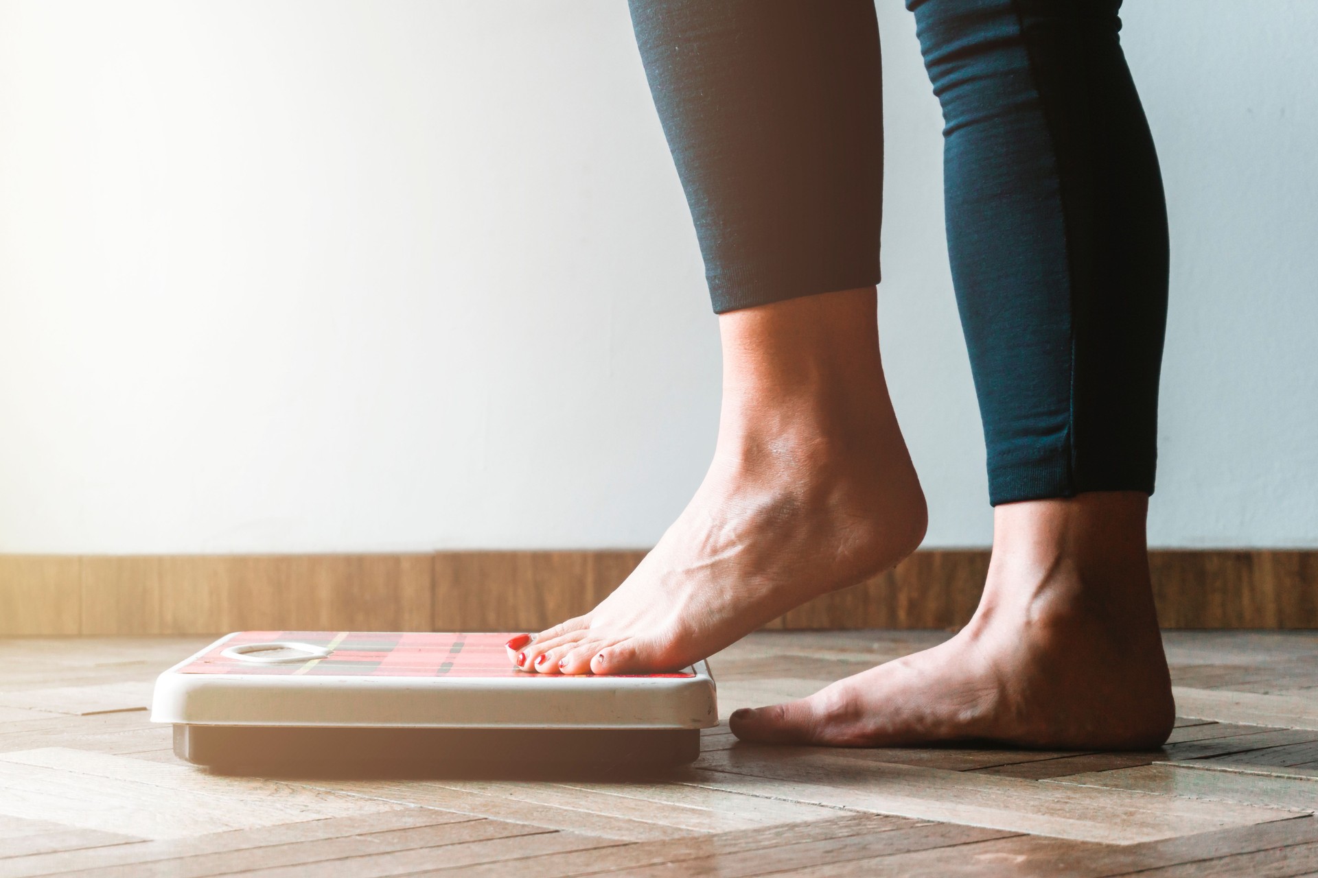 Female checking kilogrammes getting on the scale - self care and body positivity concept - warm flare on left